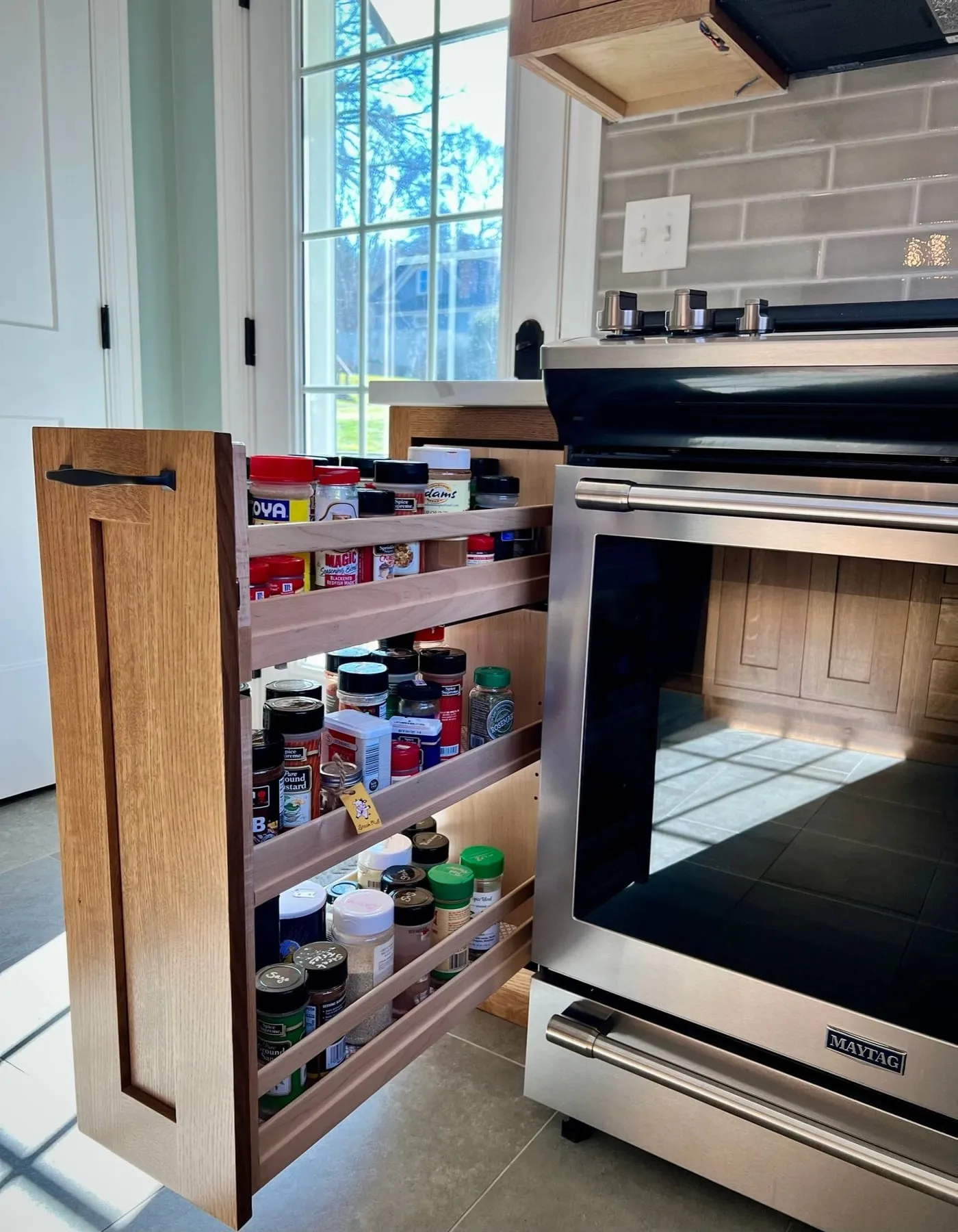 Pull-out spice rack beside the range in a white oak kitchen